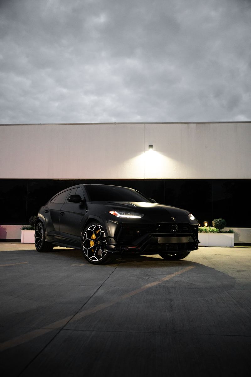 Black Lamborghini Urus under a single wall light at night