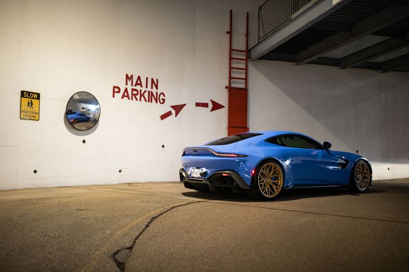 Blue Aston Martin Vantage on gold wheels in a stark parking structure