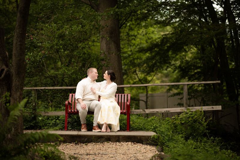 Couple close together on a red bench in the woods