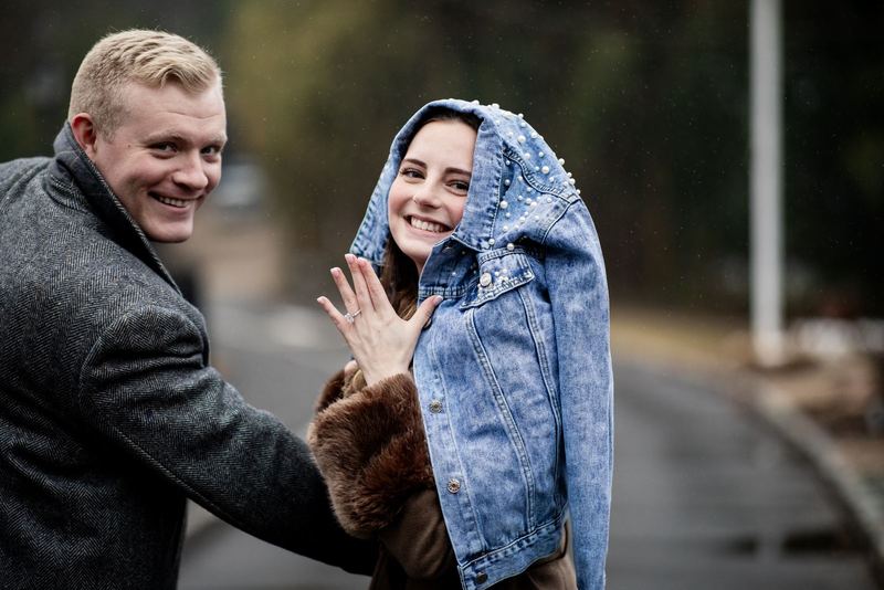 Newly engaged couple smiling as she shows her ring