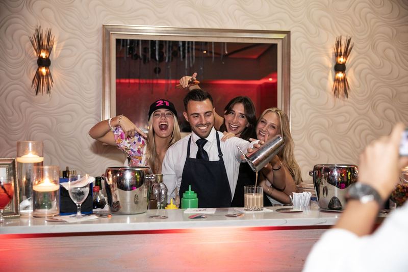Friends behind the bar pouring cocktails mid-celebration