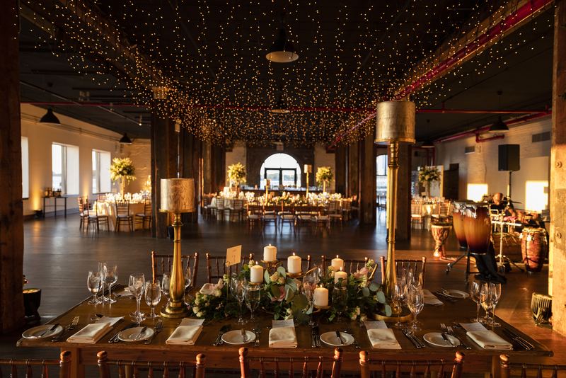 Reception hall glowing under string lights, tables dressed with candles
